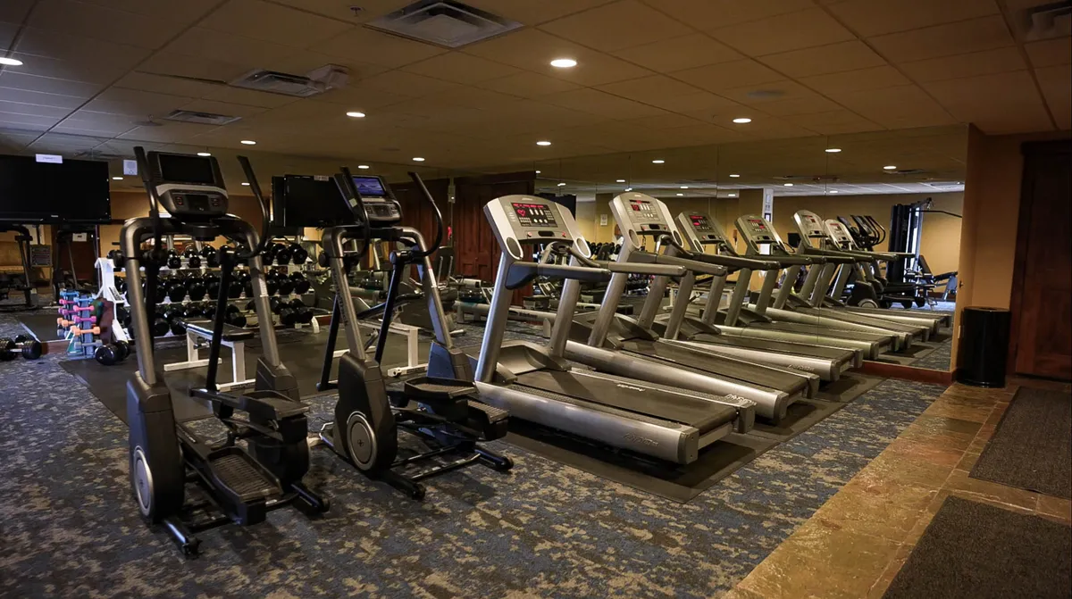 A modern fitness area with treadmills, elliptical machines, free weights, and a mirrored wall, fostering an energetic and motivating environment for workouts without leaving the building.