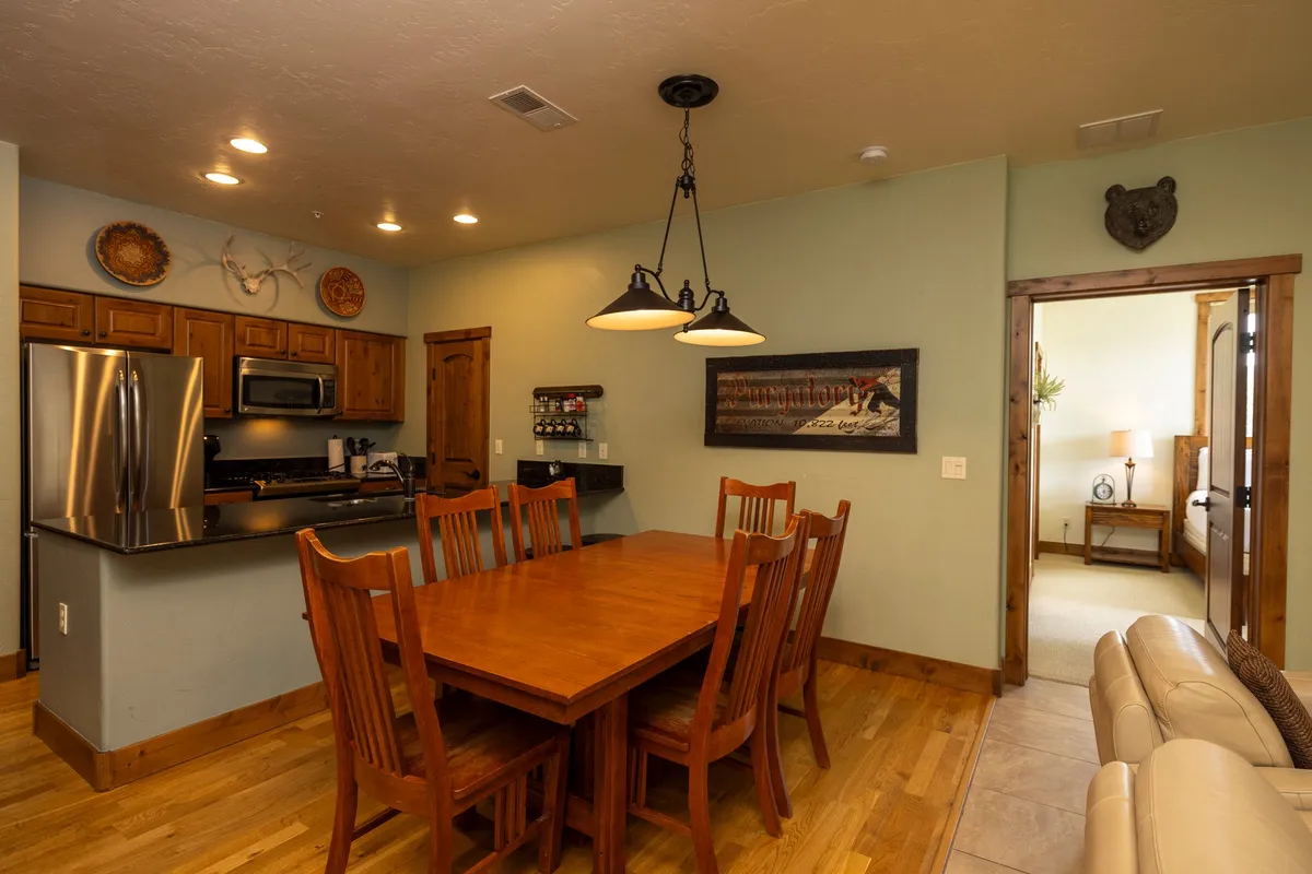 An inviting view of a dining table adjacent to the kitchen, complemented by tasteful artwork on the wall. The setup is clearly designed for family meals, gatherings, and creating special memories in a warm, communal environment.