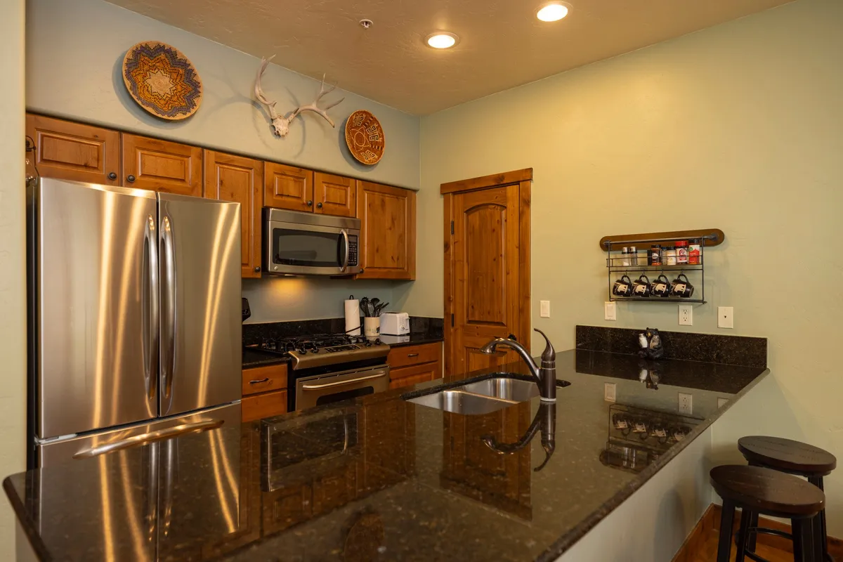 A cozy, rustic kitchen featuring stainless steel appliances, granite countertops, warm wooden cabinets, decorative plates, and antlers. The ample workspace is inviting, ideal for preparing meals and gathering around for conversation.