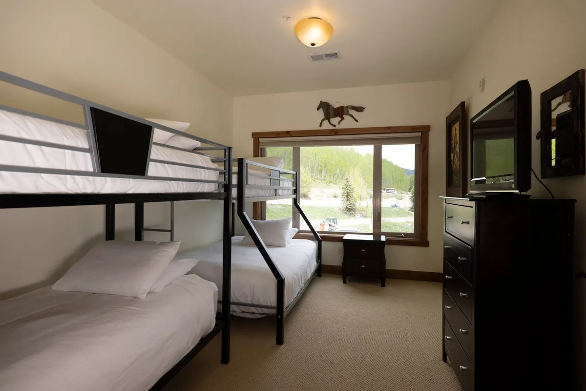 A comfortable bedroom with two sets of bunk beds, a large window offering natural light, and cozy furnishings ideal for kids or friends. The space feels playful yet inviting, perfect for memorable sleepovers or quiet time.