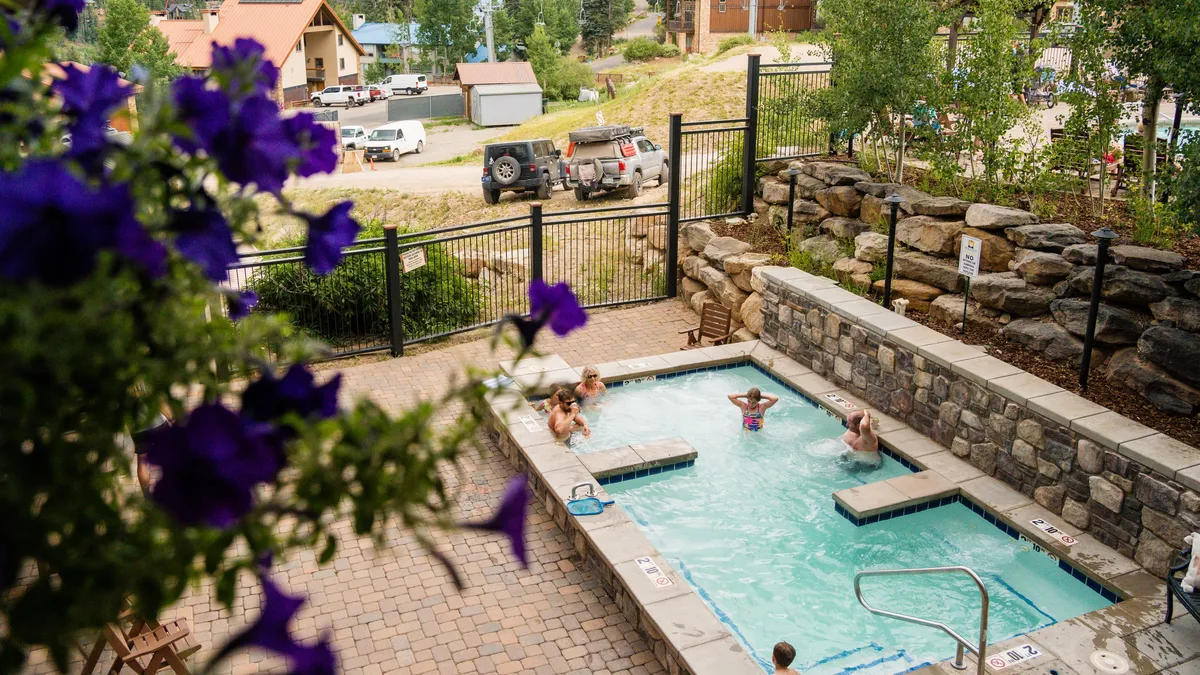 This image captures the resort's outdoor swimming pool surrounded by vibrant flowers and a stone wall. People are seen relaxing and socializing by the water, creating a lively, inviting atmosphere perfect for groups. The sunlit setting suggests opportunities for both daytime fun and relaxing evenings under the trees.