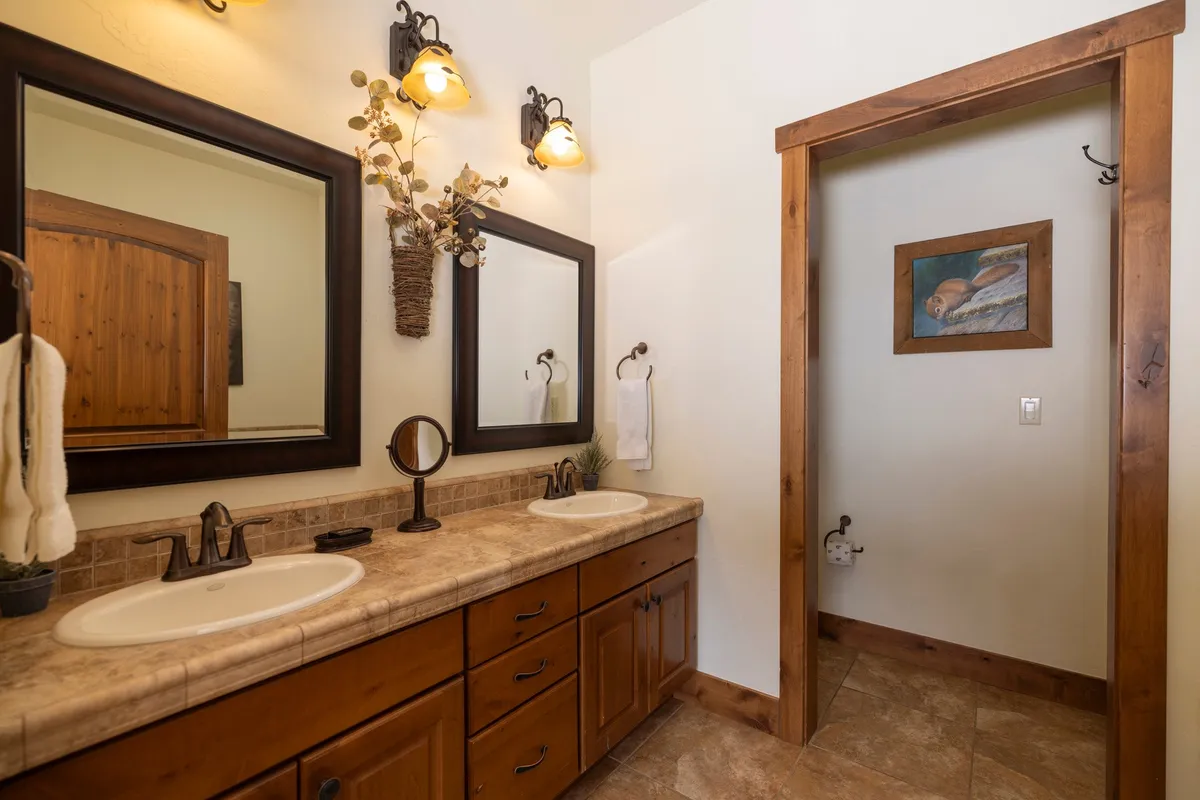 A modern bathroom with a double sink vanity, large mirrors, and decorative wall art. The atmosphere is calm and rejuvenating, perfect for self-care routines and unwinding after mountain adventures.