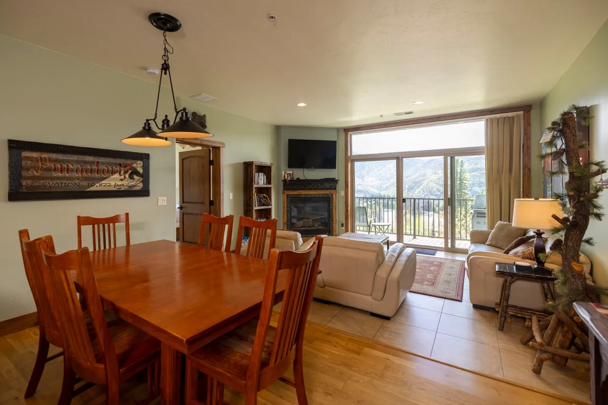 A thoughtfully arranged living and dining area featuring a comfortable seating group, a stylish dining table, and large picture windows that overlook the mountains. The fireplace adds to the cozy ambiance, inviting guests to unwind after a day outdoors.